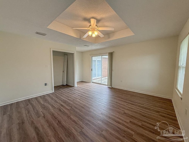 empty room featuring a textured ceiling, a tray ceiling, dark hardwood / wood-style floors, and ceiling fan