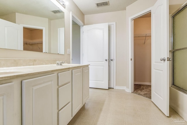 bathroom with vanity, a textured ceiling, and combined bath / shower with glass door