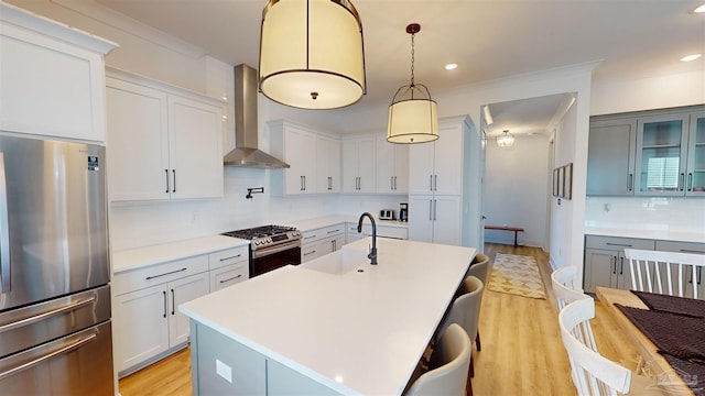 kitchen featuring sink, wall chimney exhaust hood, stainless steel appliances, a kitchen island with sink, and light wood-type flooring