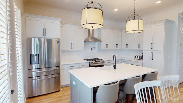 kitchen featuring sink, hanging light fixtures, wall chimney exhaust hood, an island with sink, and stainless steel appliances