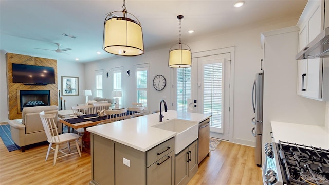 kitchen with pendant lighting, light hardwood / wood-style flooring, ceiling fan, an island with sink, and stainless steel appliances