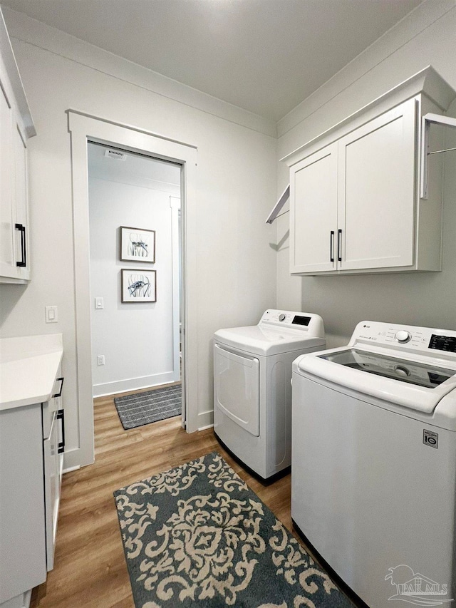 laundry room with cabinets, wood-type flooring, separate washer and dryer, and crown molding