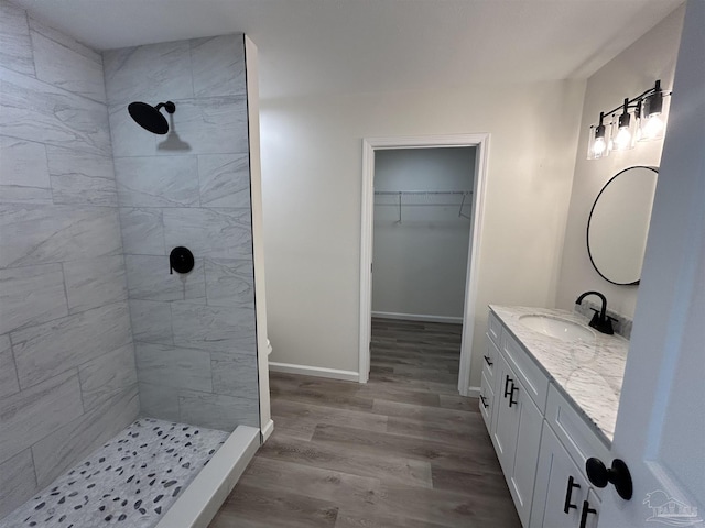 bathroom with baseboards, tiled shower, wood finished floors, a walk in closet, and vanity