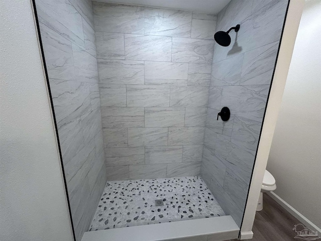 bathroom featuring toilet, a stall shower, baseboards, and wood finished floors