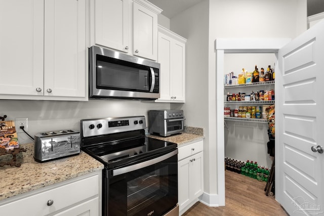 kitchen featuring light stone countertops, a toaster, wood finished floors, white cabinets, and appliances with stainless steel finishes