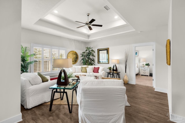 living room with dark wood-type flooring, visible vents, a ceiling fan, a raised ceiling, and baseboards
