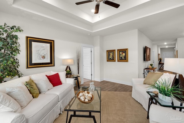 living area with light wood finished floors, a ceiling fan, baseboards, a raised ceiling, and recessed lighting