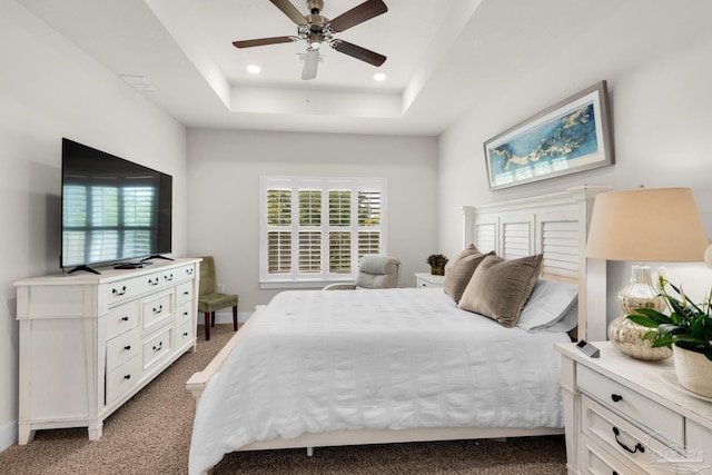 carpeted bedroom with a ceiling fan, multiple windows, a raised ceiling, and recessed lighting