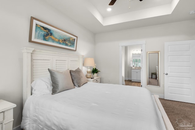 carpeted bedroom featuring a tray ceiling, ensuite bath, ceiling fan, and recessed lighting