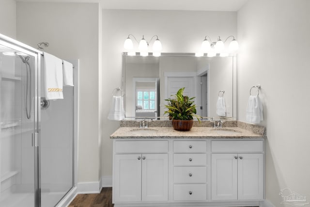bathroom featuring double vanity, wood finished floors, a stall shower, and a sink