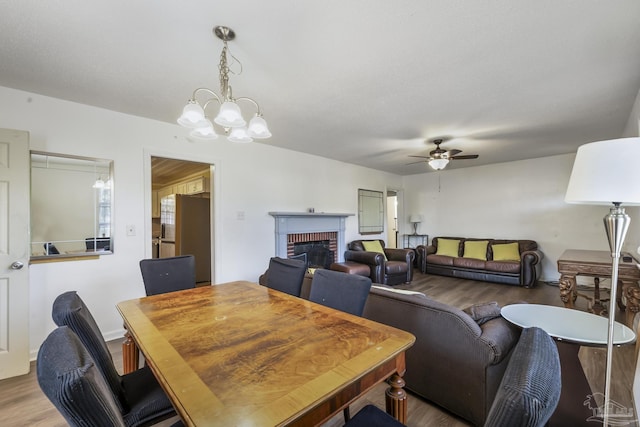 dining space with a fireplace, wood finished floors, and ceiling fan with notable chandelier