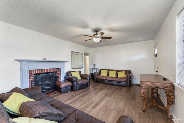 living room with ceiling fan, a textured ceiling, a brick fireplace, and wood-type flooring