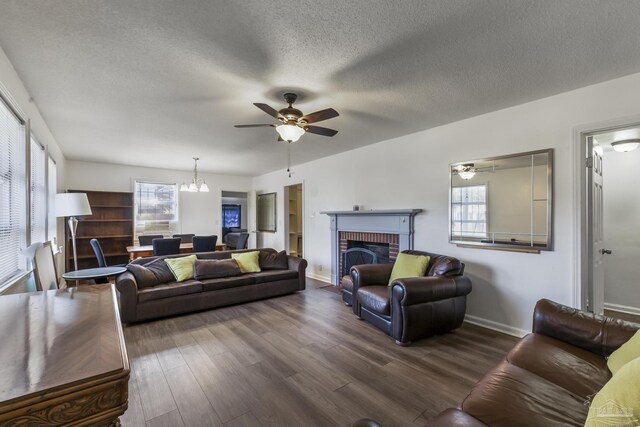 living room featuring ceiling fan with notable chandelier, wood-type flooring, a textured ceiling, and a brick fireplace