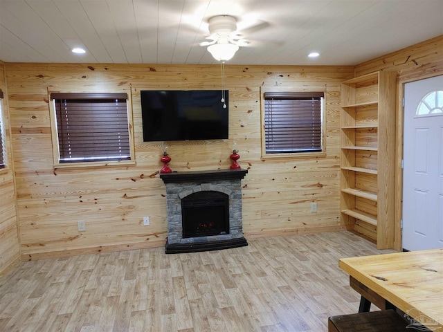 unfurnished living room featuring ceiling fan, a stone fireplace, hardwood / wood-style floors, and wooden walls