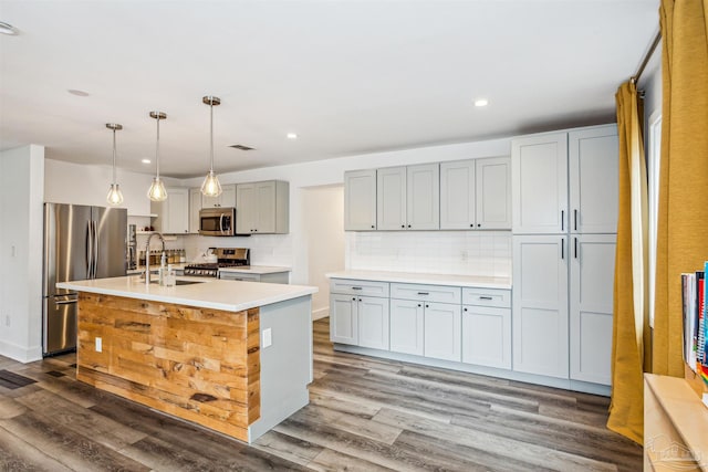 kitchen with dark hardwood / wood-style flooring, stainless steel appliances, sink, pendant lighting, and a center island with sink