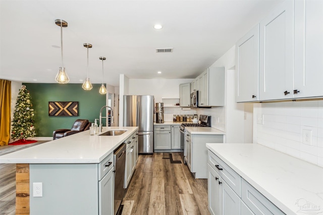 kitchen with light hardwood / wood-style flooring, sink, pendant lighting, a center island with sink, and stainless steel appliances