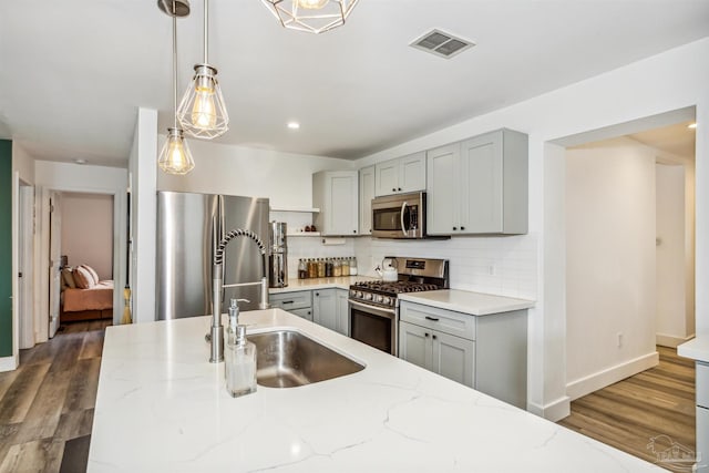 kitchen with light stone countertops, pendant lighting, stainless steel appliances, and sink