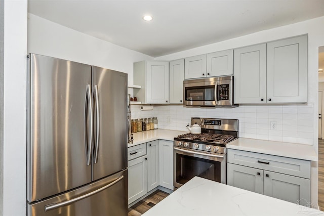 kitchen featuring gray cabinetry, decorative backsplash, appliances with stainless steel finishes, dark wood-type flooring, and light stone countertops