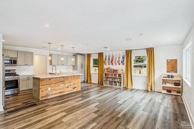 kitchen with gray cabinetry, sink, stainless steel appliances, dark hardwood / wood-style floors, and an island with sink