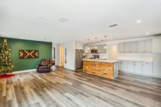 kitchen with a center island with sink, light hardwood / wood-style floors, stainless steel appliances, and pendant lighting