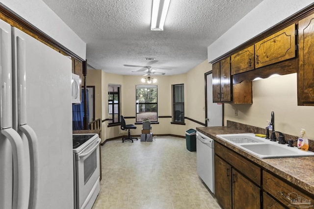 kitchen with dark countertops, light floors, white appliances, a textured ceiling, and a sink