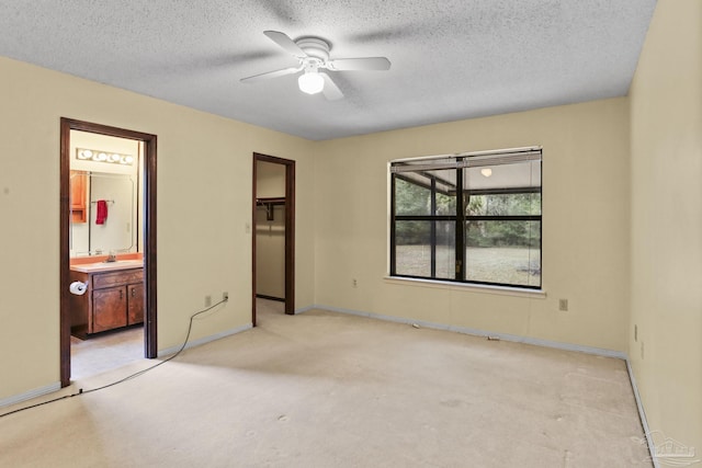 unfurnished bedroom featuring light carpet, a textured ceiling, ensuite bath, and a closet