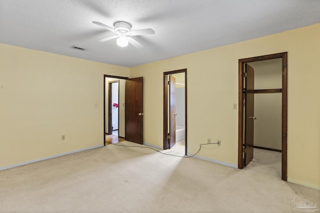 unfurnished bedroom with visible vents, a walk in closet, light carpet, ensuite bath, and a textured ceiling