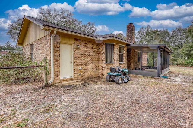 back of property with brick siding, a chimney, a garage, and a sunroom