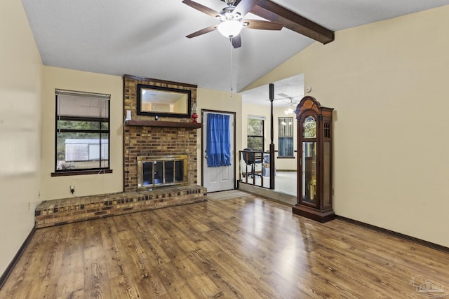 unfurnished living room with lofted ceiling with beams, wood finished floors, baseboards, a brick fireplace, and ceiling fan