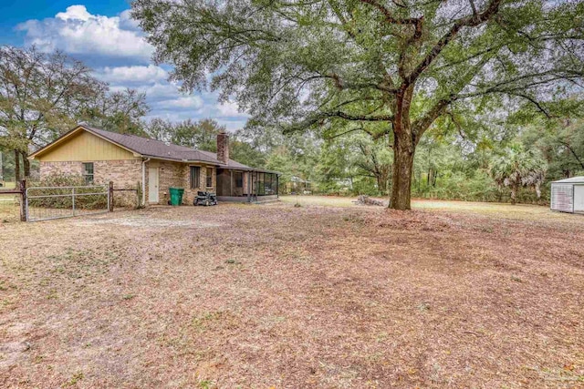 view of yard featuring an outdoor structure, a gate, a shed, and a sunroom