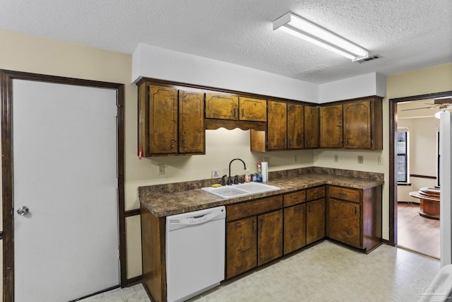 kitchen featuring dishwasher, dark countertops, light floors, and a sink