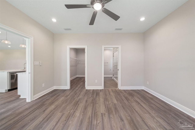 unfurnished bedroom featuring a spacious closet, a closet, ceiling fan, and wood-type flooring