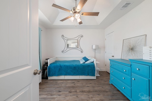 bedroom featuring a raised ceiling, a ceiling fan, wood finished floors, and visible vents