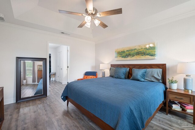 bedroom with visible vents, ornamental molding, wood finished floors, baseboards, and a raised ceiling