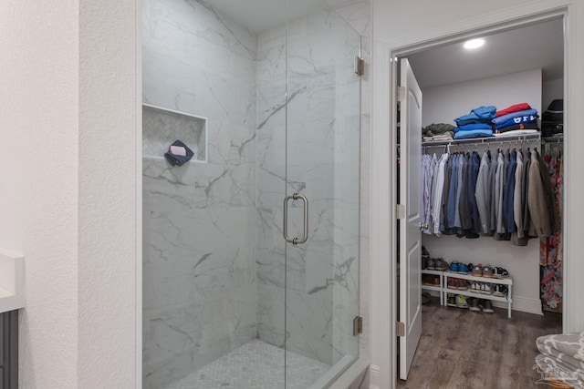 full bath featuring a marble finish shower, a walk in closet, and wood finished floors