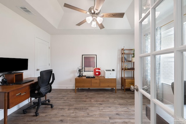office space with ceiling fan, baseboards, wood finished floors, a tray ceiling, and visible vents
