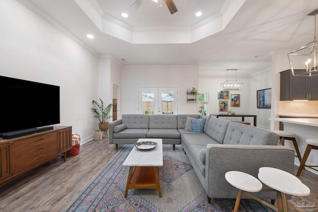 living area with a raised ceiling, ceiling fan with notable chandelier, recessed lighting, wood finished floors, and ornamental molding