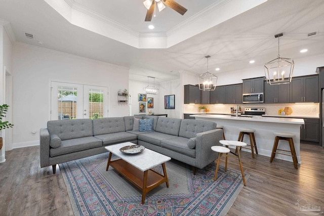 living area with ceiling fan with notable chandelier, a tray ceiling, dark wood-type flooring, and visible vents