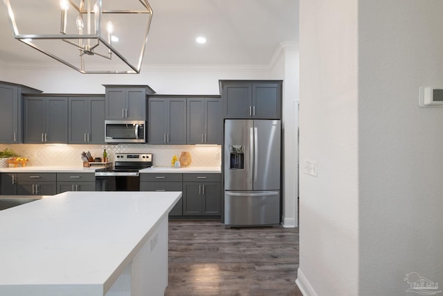 kitchen with a chandelier, dark wood finished floors, stainless steel appliances, decorative backsplash, and ornamental molding