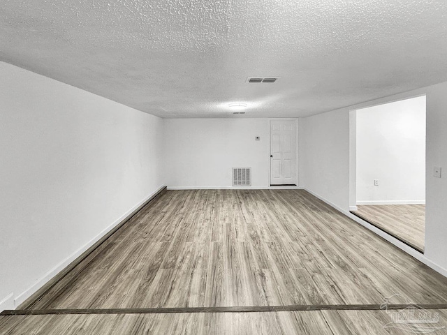 spare room featuring a textured ceiling, wood finished floors, visible vents, and baseboards