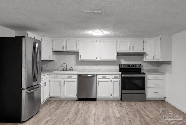 kitchen featuring light wood finished floors, appliances with stainless steel finishes, under cabinet range hood, white cabinetry, and a sink