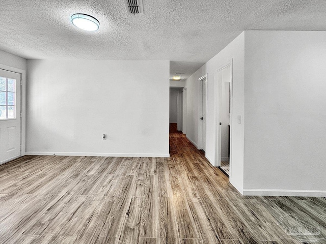 unfurnished room with a textured ceiling, wood finished floors, visible vents, and baseboards