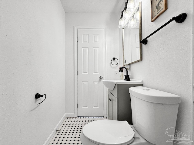 half bathroom with a textured wall, vanity, toilet, and baseboards