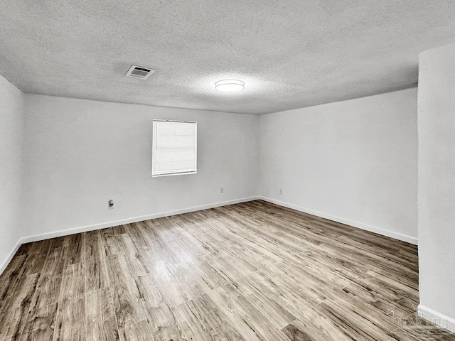 empty room with baseboards, a textured ceiling, visible vents, and wood finished floors