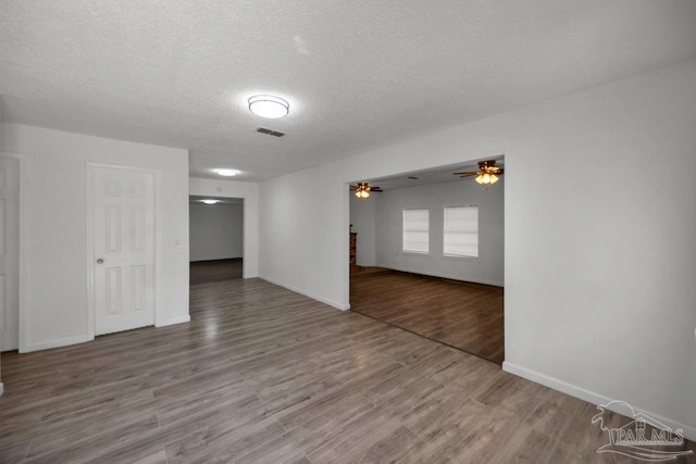 empty room featuring a textured ceiling, wood finished floors, visible vents, baseboards, and a ceiling fan