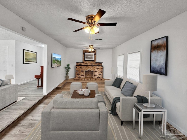 living room featuring a fireplace, visible vents, a textured ceiling, wood finished floors, and baseboards