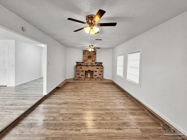 unfurnished living room with a brick fireplace, a textured ceiling, baseboards, and wood finished floors