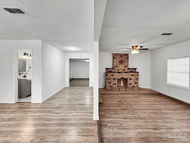 unfurnished living room with visible vents, a ceiling fan, a brick fireplace, a textured ceiling, and wood finished floors