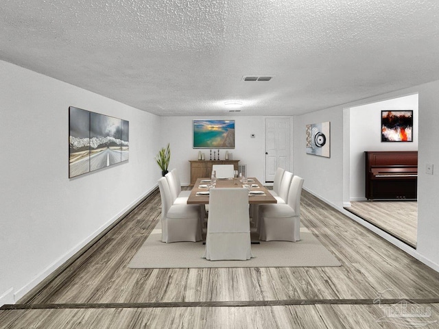 dining room with a textured ceiling, wood finished floors, visible vents, and baseboards