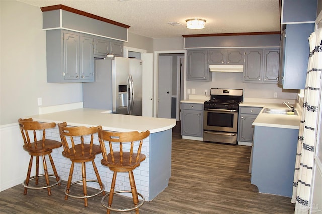 kitchen featuring a sink, a peninsula, gray cabinetry, under cabinet range hood, and stainless steel appliances